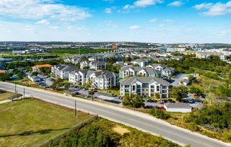 A road with a grassy area on the side and a row of houses in the distance.