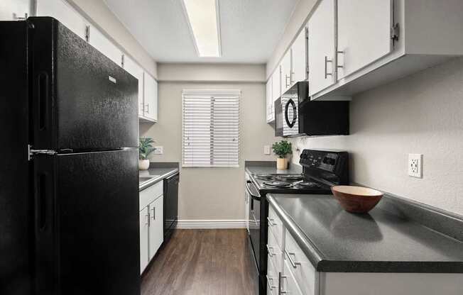 A black refrigerator is on the left in a kitchen with white cabinets.