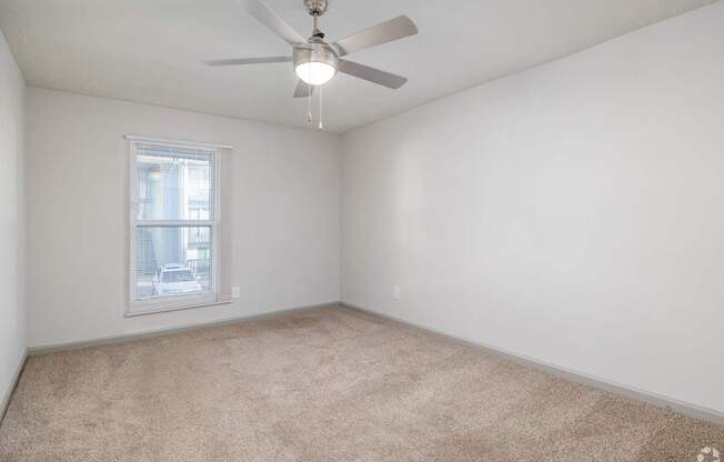 Empty room with a ceiling fan and carpeted floor.