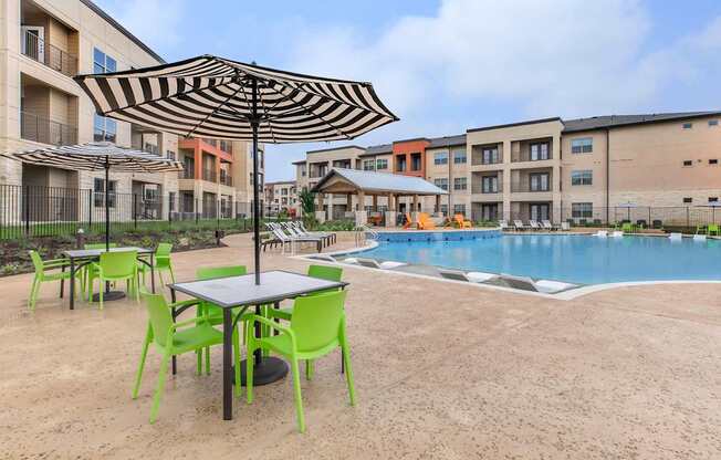 A table with a black umbrella is in the middle of a sandy area.