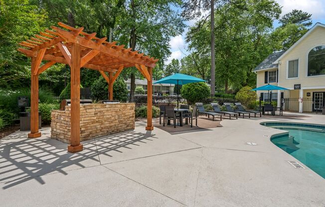a backyard with a pool and a wooden pavilion with tables and umbrellas