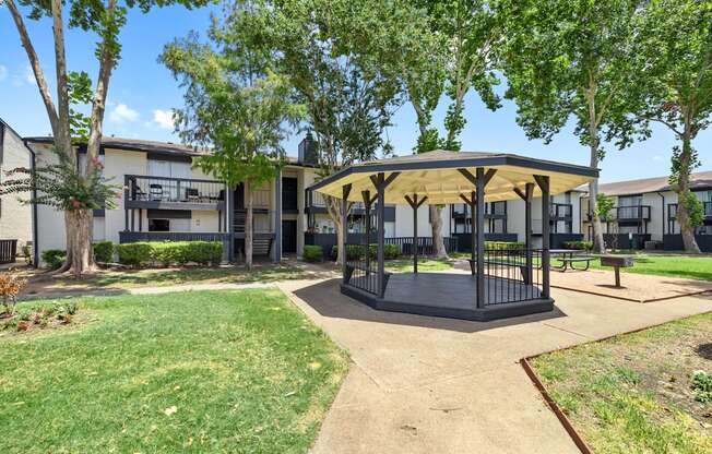 a gazebo with trees and apartments in the background