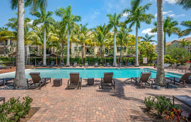 A pool surrounded by palm trees and lounge chairs.