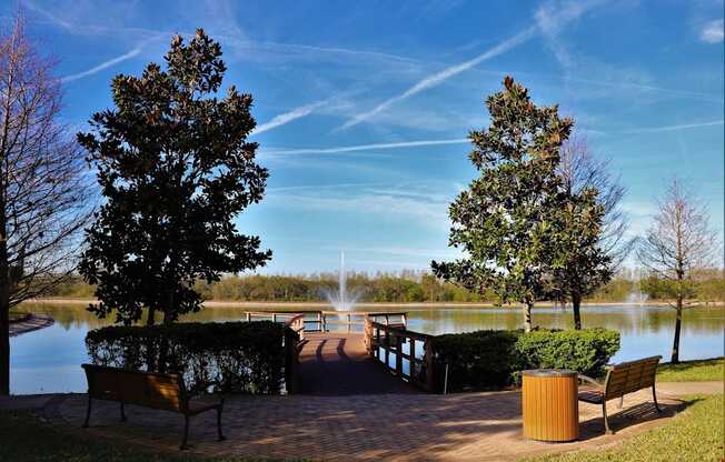 A park with a bench, a tree and a lake.