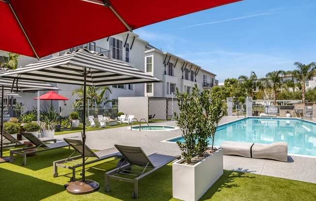 A pool area with a red umbrella and lounge chairs.