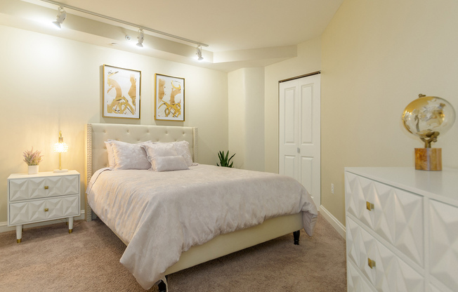 Bedroom in an apartment furnished with a queen-size bed, a nightstand, carpet flooring, and a high ceiling.