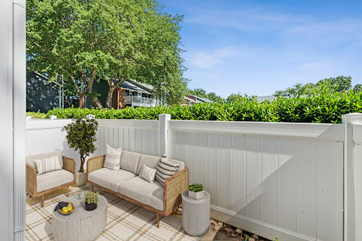 A white fence encloses a small patio with a couch, chairs, and a table.
