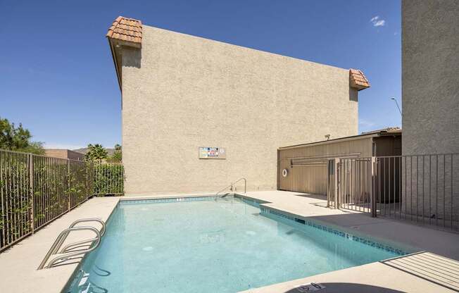 A small pool in a backyard with a tan wall and a black fence.