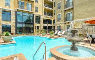a swimming pool with a fountain in front of an apartment building