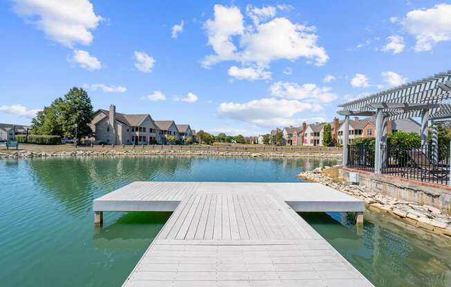 A wooden dock extends into a body of water with a residential area in the background.