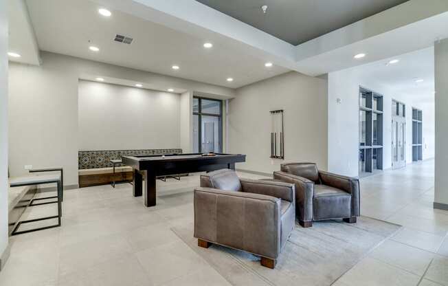 Game room in Ascend at Woodbury apartments' clubhouse with pool table and leather chairs.