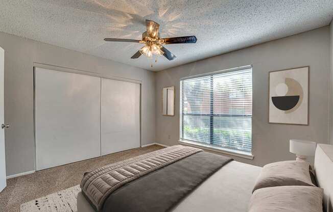 A bedroom with a bed, a ceiling fan, and a window with blinds.