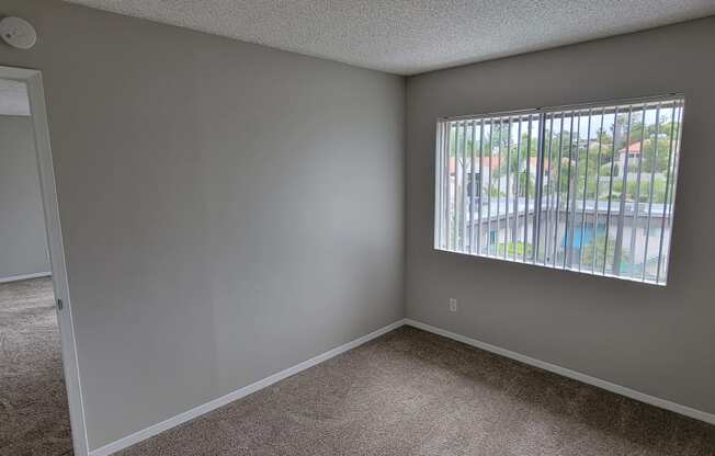 Carpeted bedroom with large window at La Mesa Village Apartments in La Mesa, California.