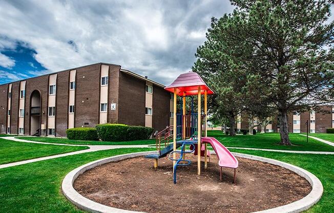 A playground with a red roof and a slide is in the foreground of a building.