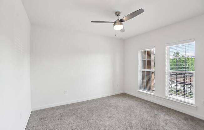 A large bedroom with a ceiling fan, windows, and carpeted floor.