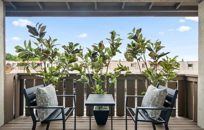 a patio with two chairs and a table on a balcony with trees in the background