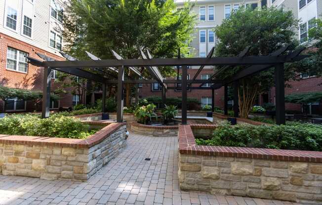 a courtyard with a pergola and a stone retaining wall with plants and trees