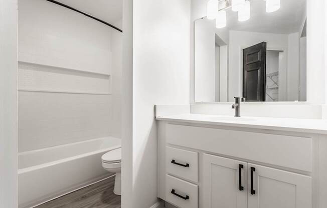 A white bathroom with a tub, sink, and mirror.