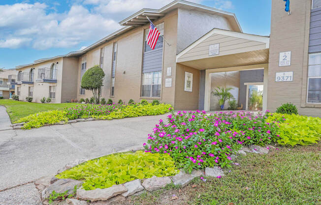 A leasing office with a US flag on it and a blooming garden bed in front  at The Creole Apartments in Shreveport, LA