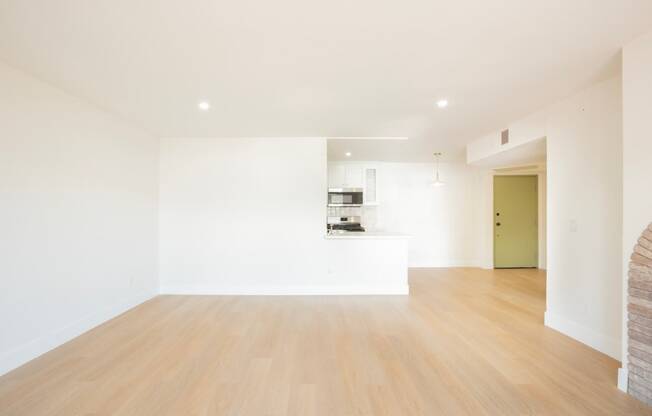 a living room and kitchen with white walls and wood floors