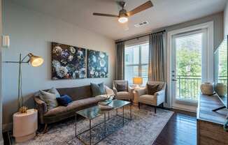 A living room with a brown couch, a glass coffee table, and a ceiling fan.