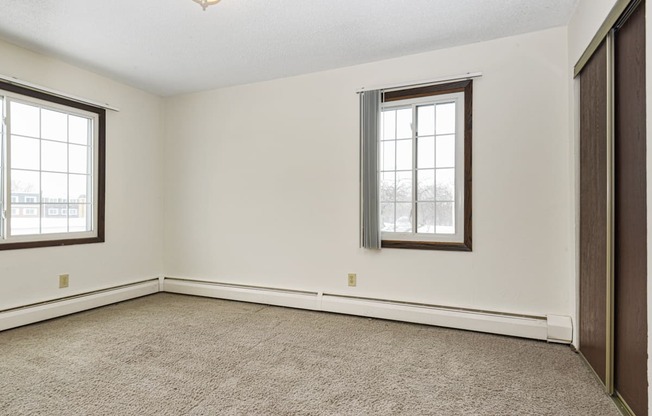 a bedroom with two windows and a carpet. Fridley, MN Georgetown on the River Apartments