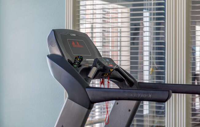 A treadmill with a digital display and control panel is placed in a room.