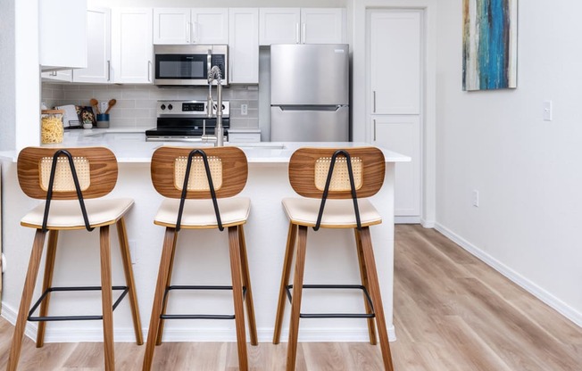 a kitchen with wooden bar stools in front of a counter with a kitchen island