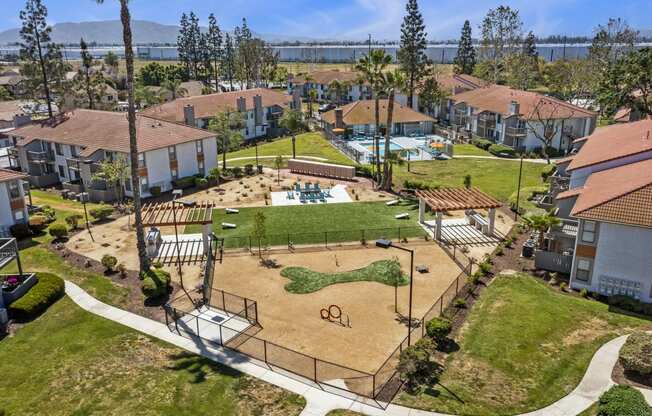 Dog-Friendly Apartments in Moreno Valley, CA - Ardella on Chagall - Aerial View of Property Grounds Showcasing Aparment Buildings, Fenced Dog Park, BBQ Area with Grilling Stations, Cornhole Playing Field, and Pool Area.