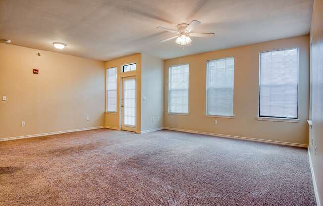 an empty living room with a ceiling fan and three windows