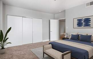 A bedroom with a bed, a bench, and a plant.