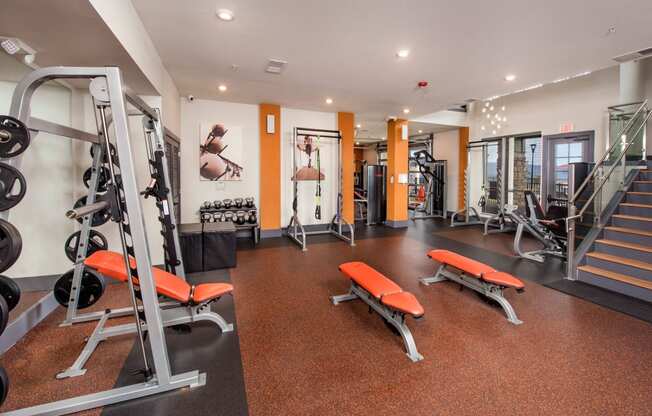 a gym with weights and cardio equipment on the floor and a staircase