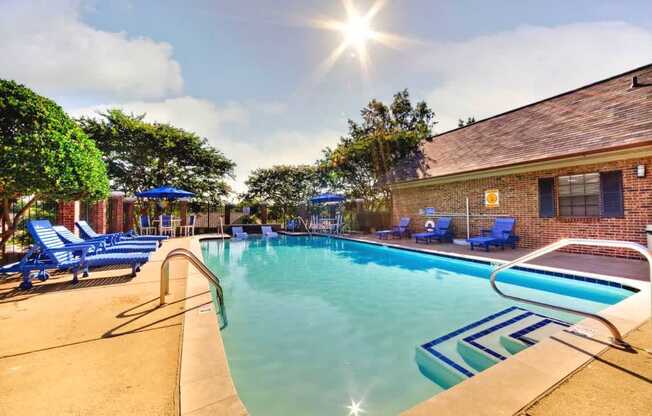 A sunny day at the pool with blue lounge chairs and a building in the background.