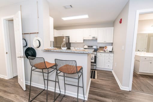 a kitchen with white cabinets and a counter top with two stools at Merion Milford Apartment Homes, CT 06460