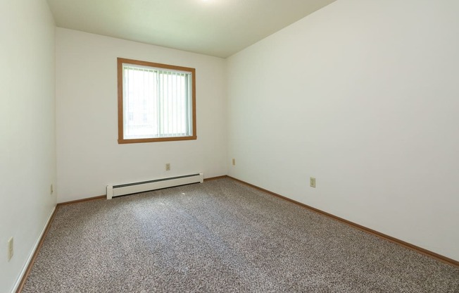 a bedroom with carpet and a window. Fargo, ND Islander Apartments