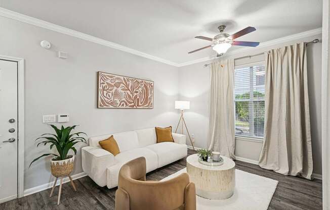 A living room with a white couch, a brown chair, and a ceiling fan.