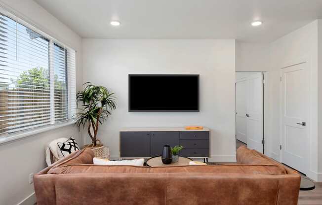 a living room with a brown couch and a tv on the wall