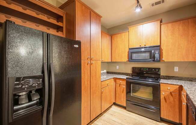 a kitchen with black appliances and wood cabinets At Metropolitan Apartments in Little Rock, AR
