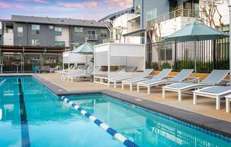 A swimming pool with sun loungers and umbrellas in front of a building.