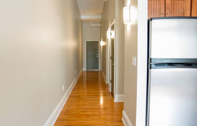 a hallway with white walls and wood floors and a stainless steel refrigerator