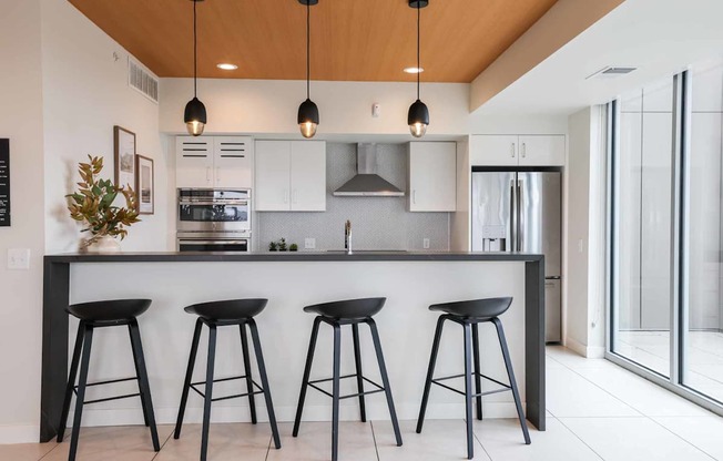 A modern kitchen with a bar area and three black stools.