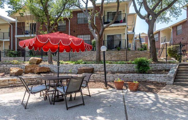 A patio with a table and chairs and a red umbrella.