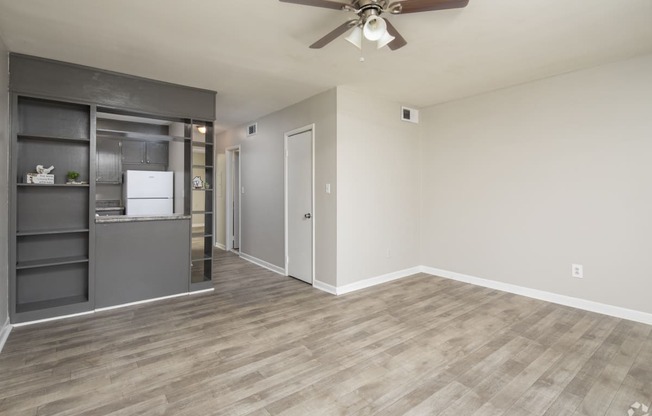 an empty living room with a ceiling fan and a kitchen