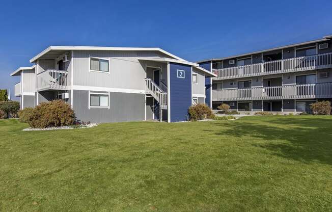 Exterior view of manicured grounds and building, and blue skies in the background at The Lakes Apartments, Moses Lake, WA.