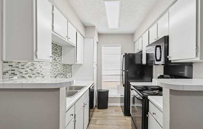 A6 kitchen with black appliances and white cabinets at Windridge on the Parkway apartments in Dallas, TX.