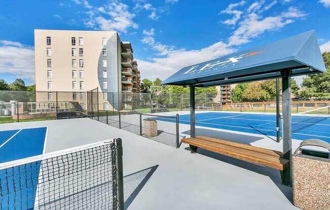 A tennis court with a blue roof and a wooden bench.