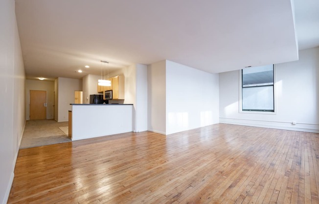 an empty living room with hardwood floors and a kitchen in the background at 26 West, Managed by Buckingham Urban Living, Indianapolis