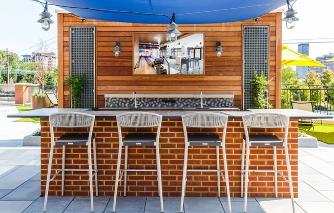 the outdoor bar is under a blue awning and a brick wall with chairs at One Ten Apartments, Jersey City , New Jersey