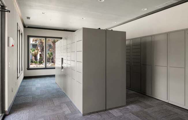 A long hallway with a row of lockers on the right and a window with a view of trees on the left.