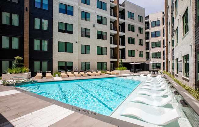 A pool surrounded by buildings and lounge chairs.